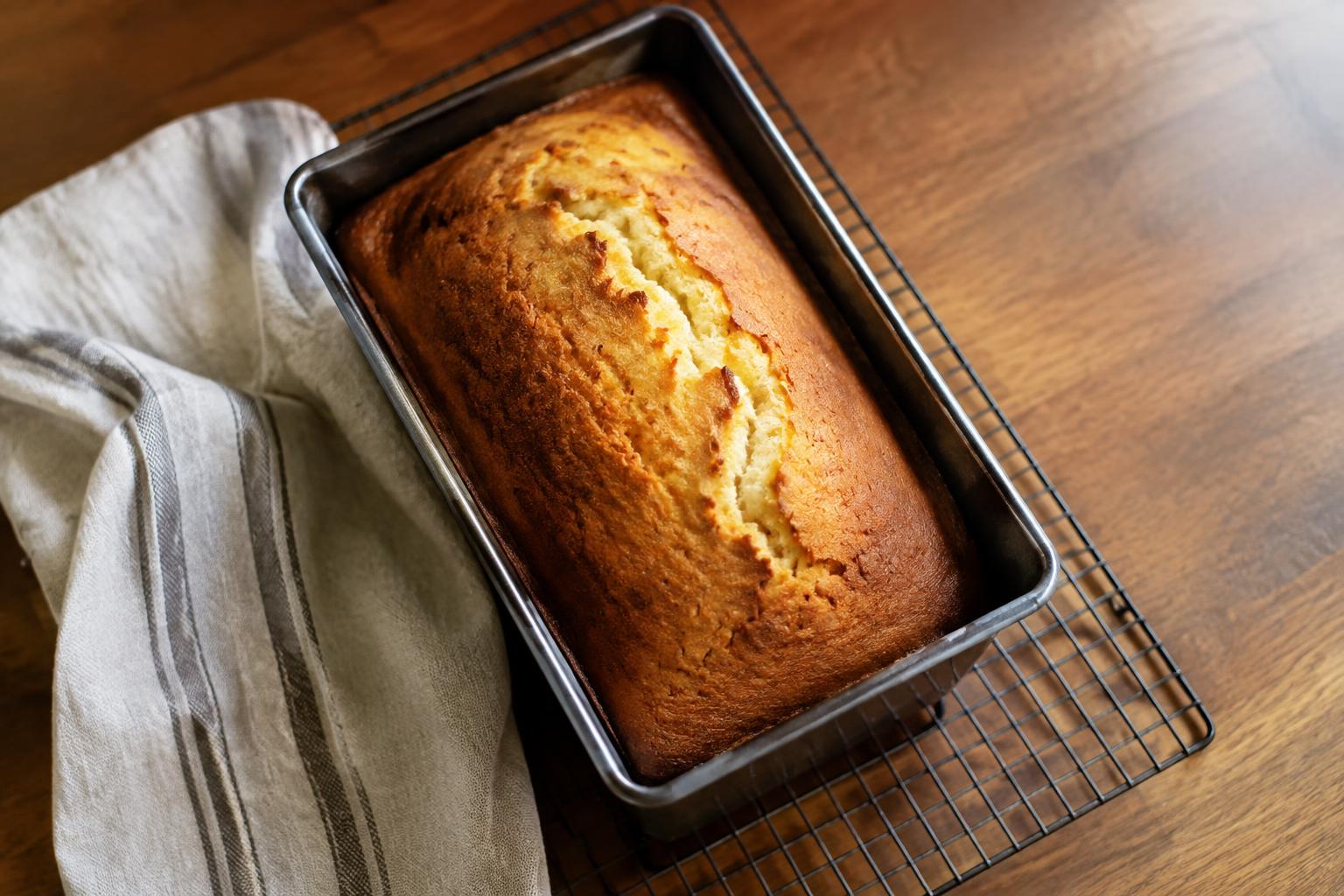 A golden loaf cake cooling in its pan on a wire rack